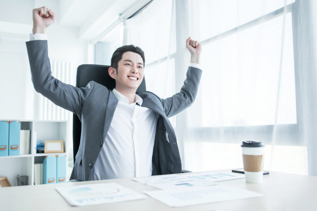 Portrait of excited Asian man holding hands folded in elbows and screaming in joy against white background. Concept of success